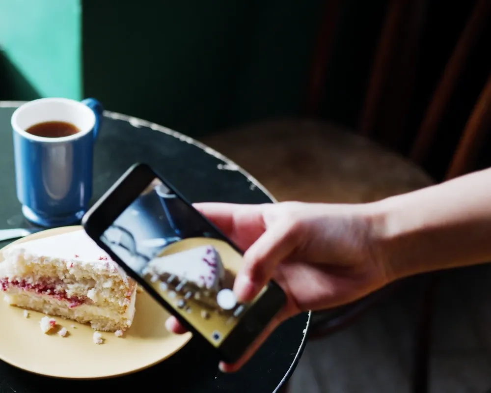 Kafe masasında pastasının fotoğrafını telefonuyla çeken bir misafir